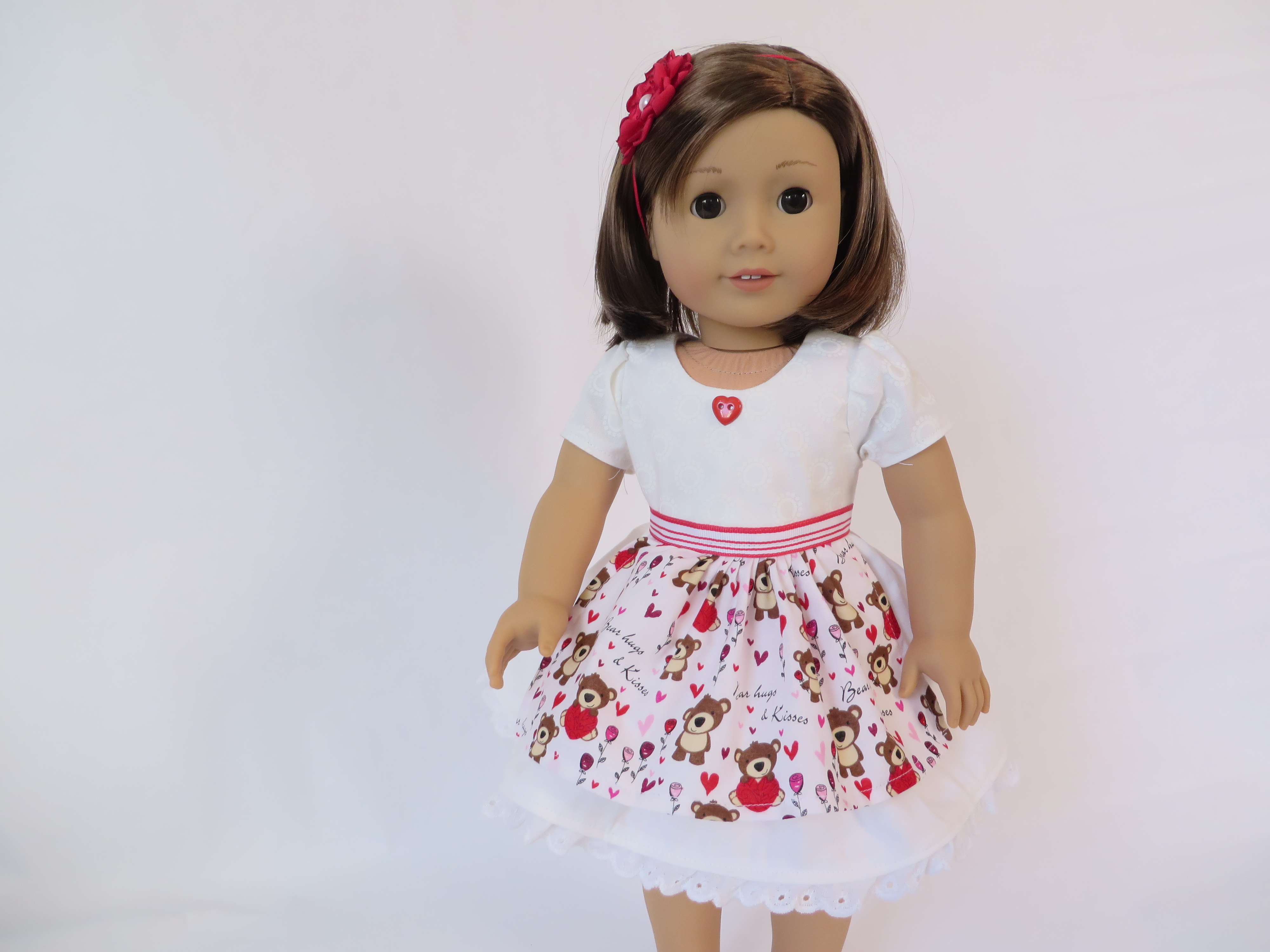 Make a cute dress for your 18 inch doll for Valentine's day. The Sugar n Spice PDF sewing pattern's white dress can be worn for any holiday with a cute apron over the top. Find the Oh Sew Kat! pattern on Etsy. #valentinesdaydress #18inchdolls #americangirl #sewingpattern #ohsewkat